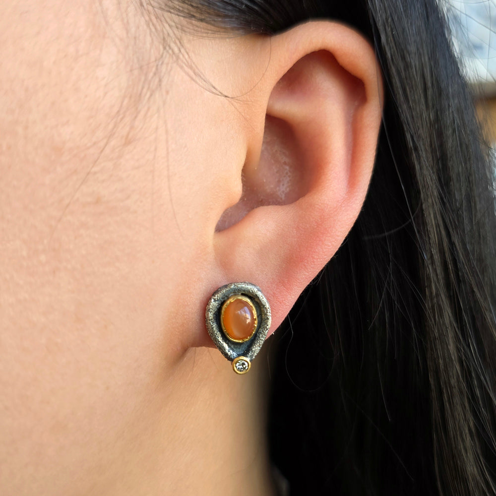 Woman wearing peach cat-eye moonstone stud earrings with oxidized silver and gold detailing from Alara Jewelry
