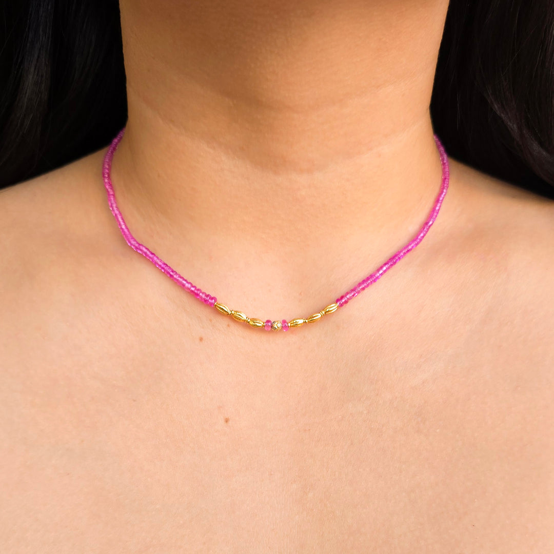 Pink sapphire strand necklace with diamond-accented center bead worn by a woman