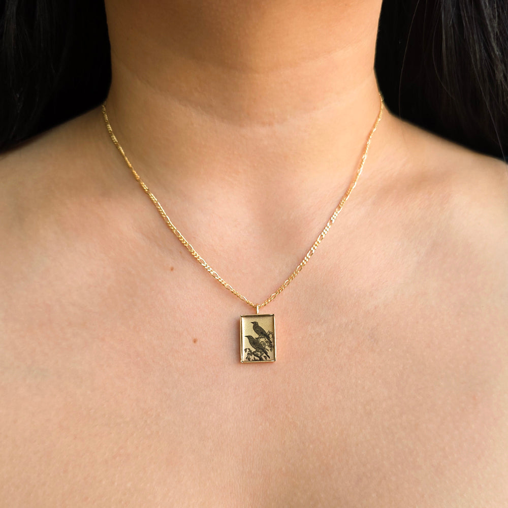 Close-up of hand-illustrated crow detail on rectangular pendant
