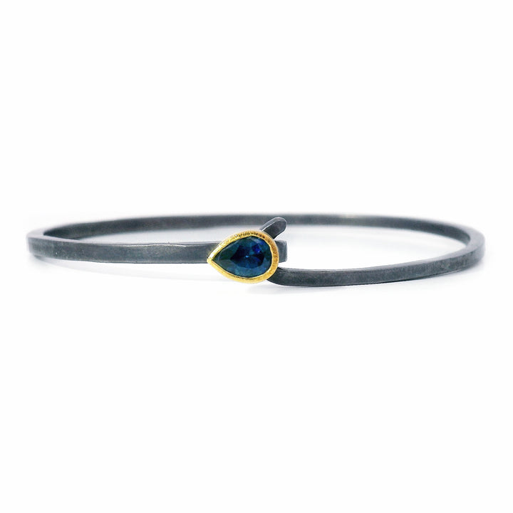 Close-up of pear-cut blue Montana sapphire set in gold bezel on silver bracelet