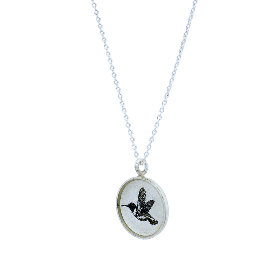Close-up of hand-etched hummingbird illustration on round pendant