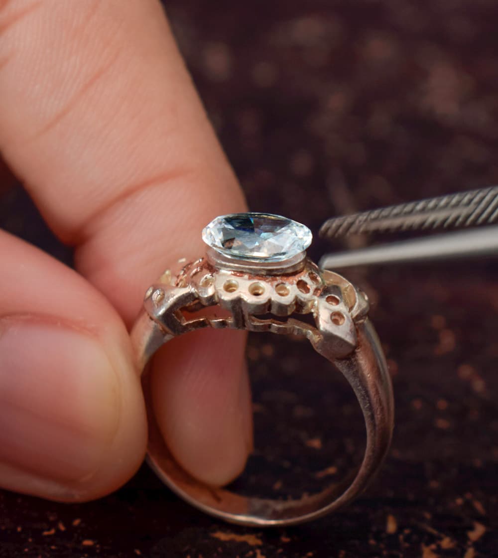 Close up of a jeweler adding a center stone to a ring